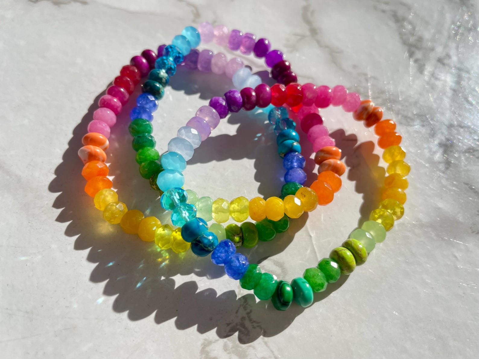 Stack of rainbow gemstone candy bracelets on marble