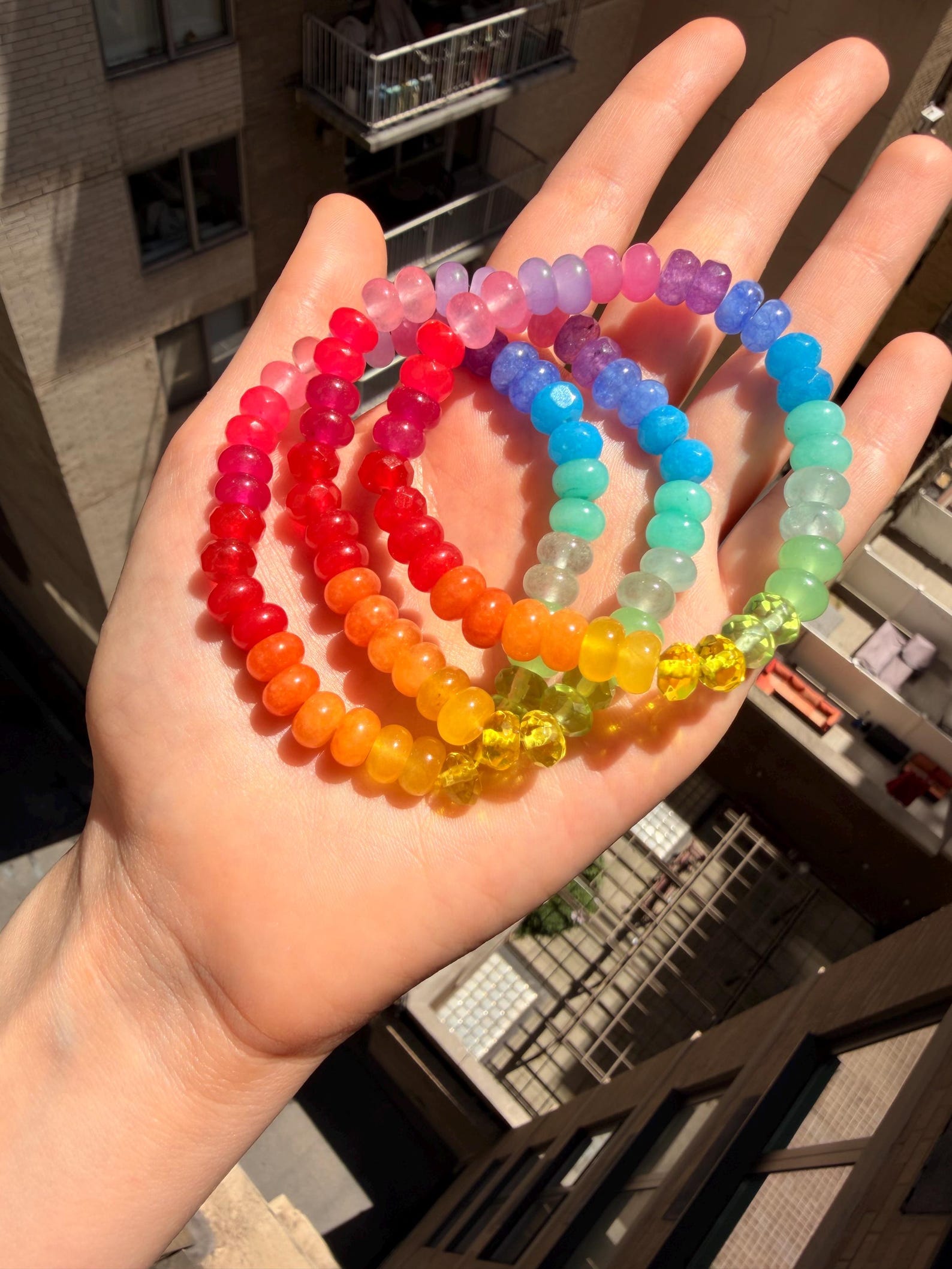 Amanda holding a handful of rainbow gemstone bracelets above a NYC courtyard